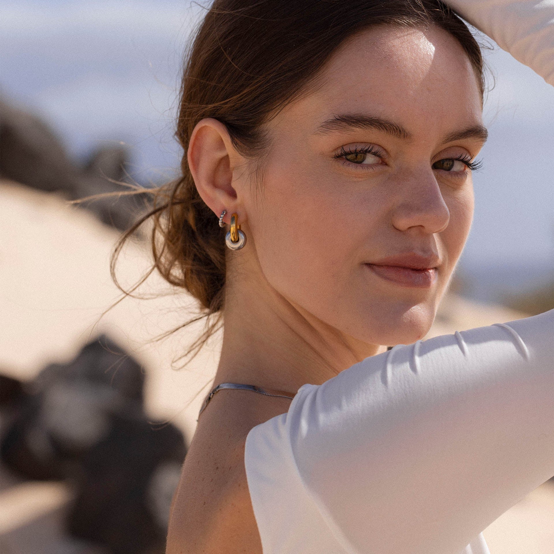 Silberne Creolen mit modernem Design, getragen von einer Frau im Sonnenlicht – PURELEI.