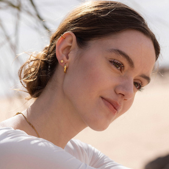 Roségoldene Ohrringe mit Sonnenmotiv, PURELEI, in sonniger, entspannter Atmosphäre.