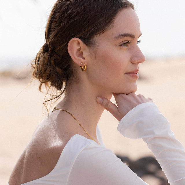 Roségoldene Creolen und zarte Kette von PURELEI, elegant und feminin am Strand getragen.