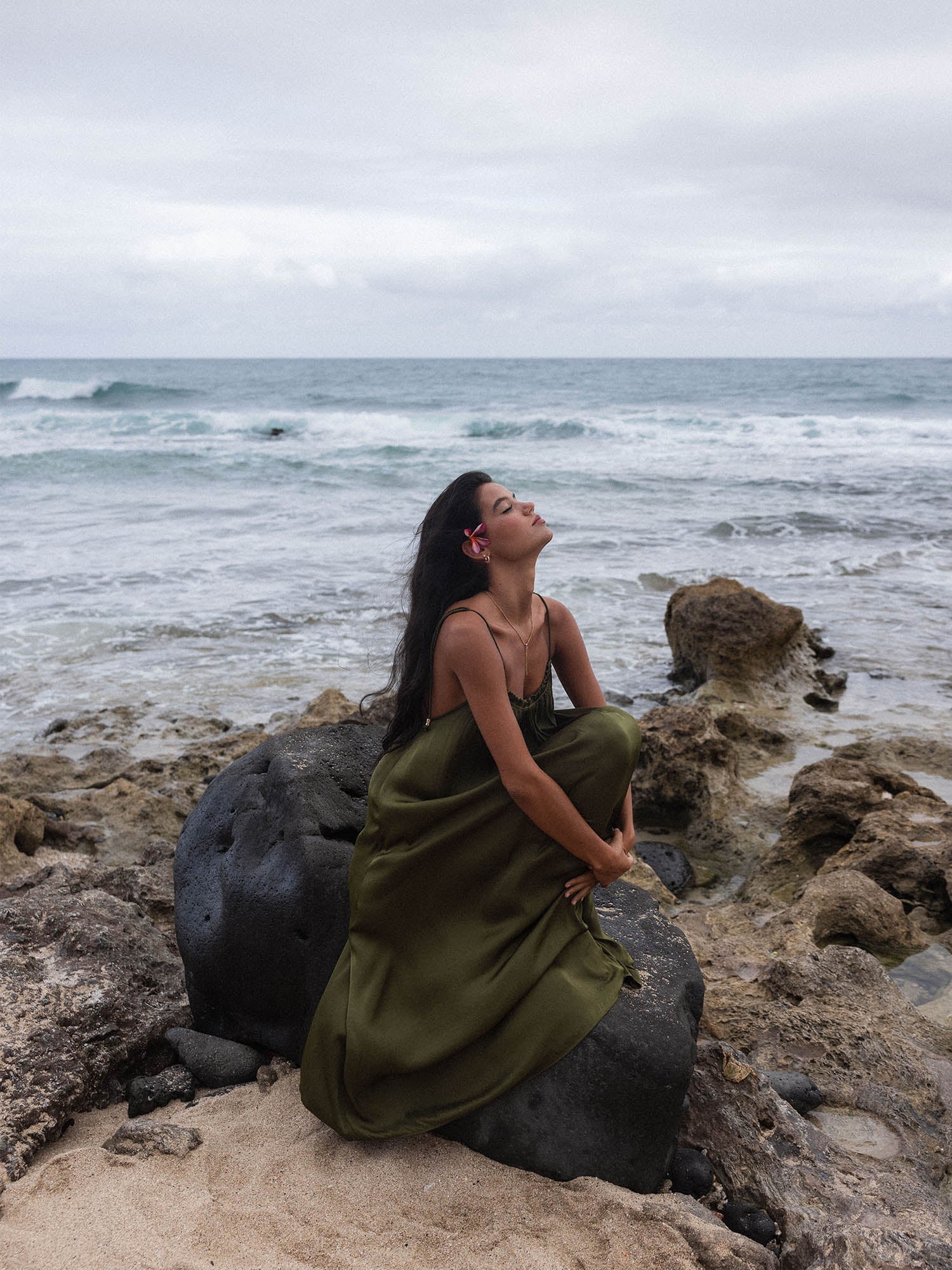 Frau in braunem Kleid am Strand, umgeben von Felsen, inspiriert von PURELEI.