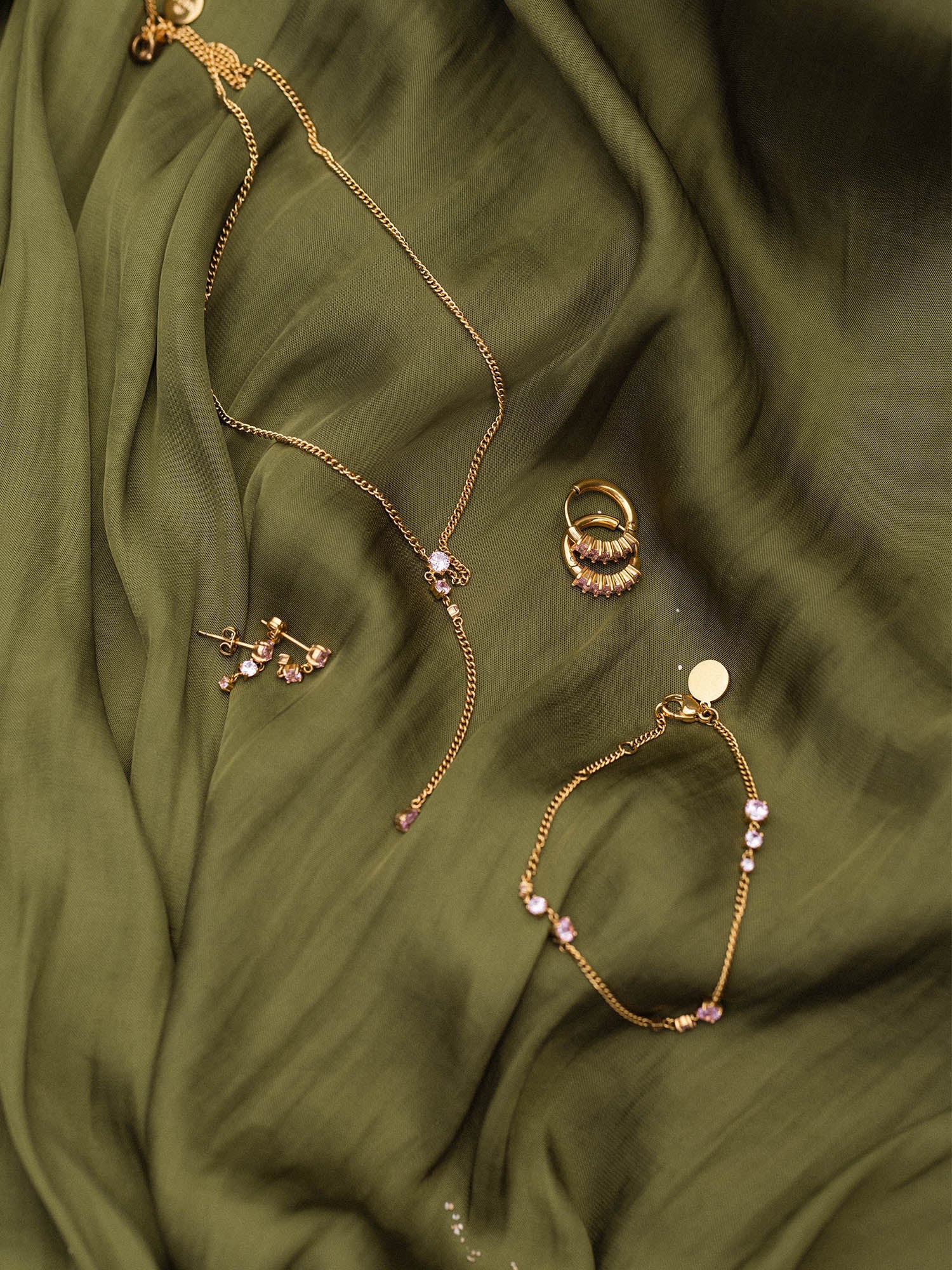 Zarte goldene Schmuckstücke von PURELEI auf grünem Stoff, elegant und feminin.