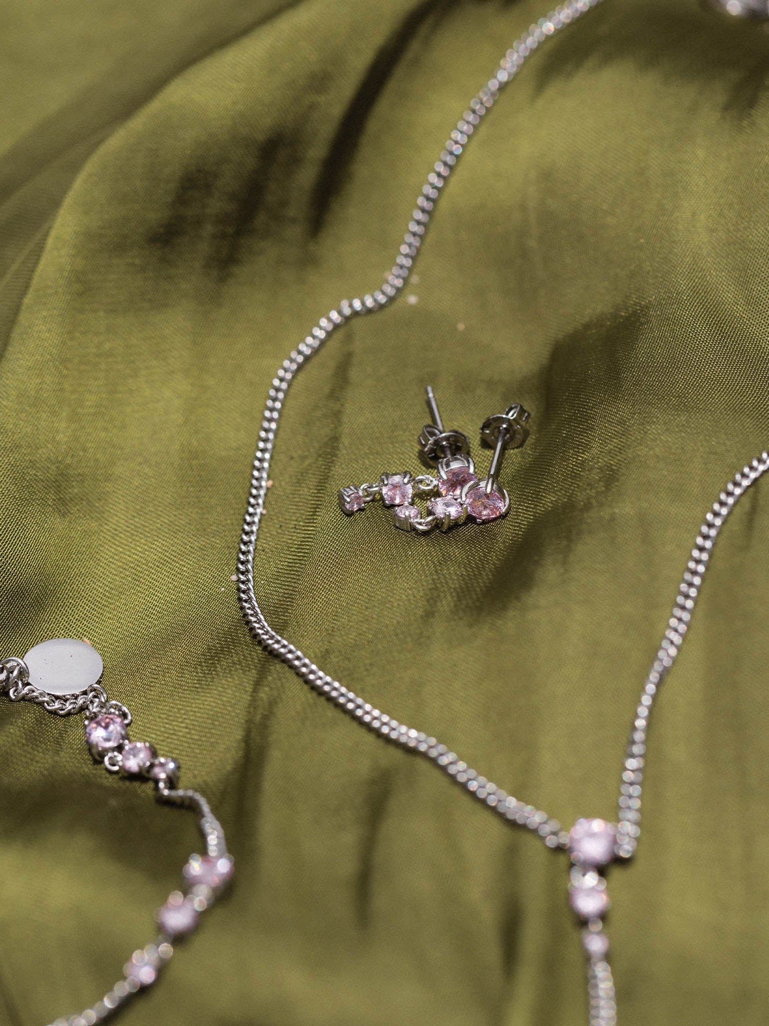 Silberne Ohrringe und Ketten auf grünem Stoff, PURELEI inspiriert.