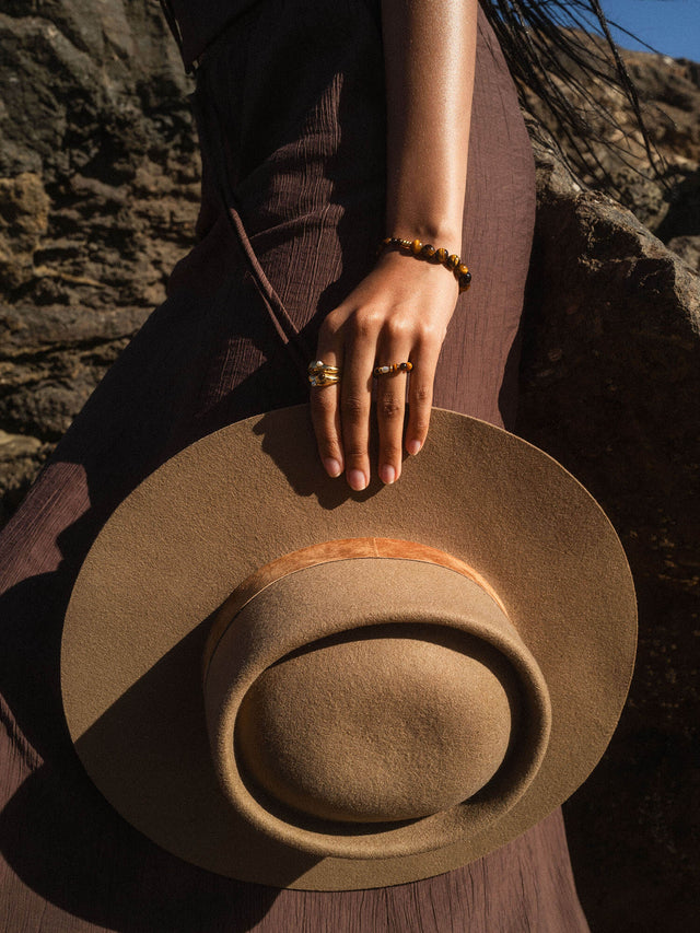 Braune PURELEI Ringe und Armband, getragen mit einem Hut in warmem Licht.