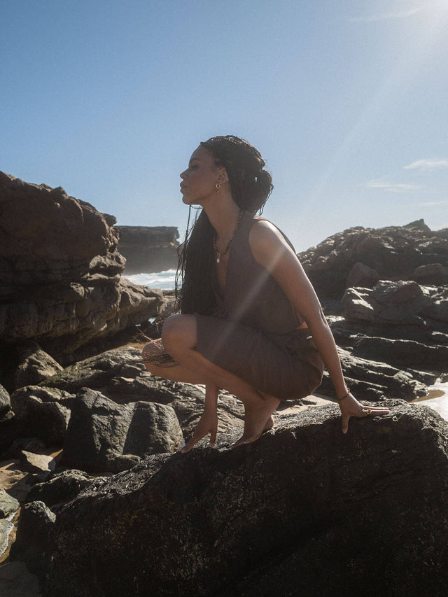 Frau in grauem Outfit auf Felsen, strahlender Himmel, PURELEI inspiriert.