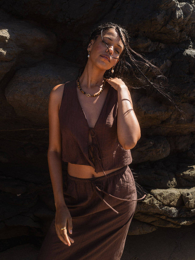 Braune, natürliche Schmuckstücke von PURELEI, getragen vor Felsen, strahlen entspannte Eleganz aus.