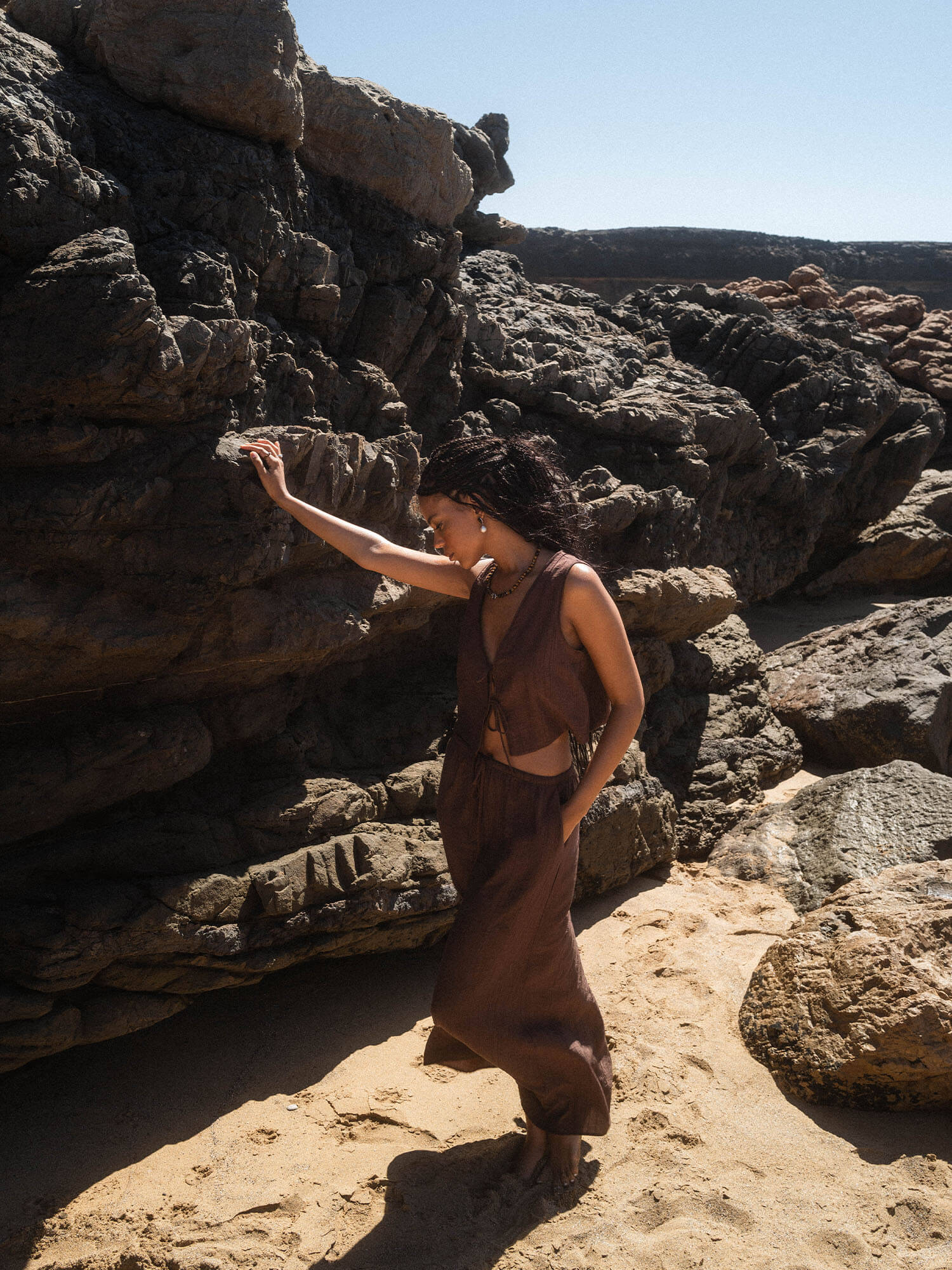 Braunes, luftiges Outfit am Strand, umgeben von Felsen, inspiriert von PURELEI.