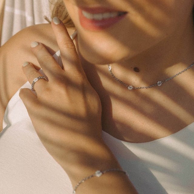 Silberne Kette und Ring mit blütenförmigen Details, PURELEI, in warmem Licht.