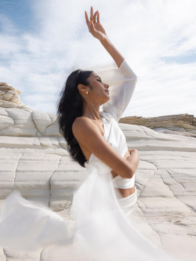 Eleganter PURELEI Gemini Letter Charm aus goldfarbenem Edelstahl, getragen vor hellem Fels, urbane Leichtigkeit.