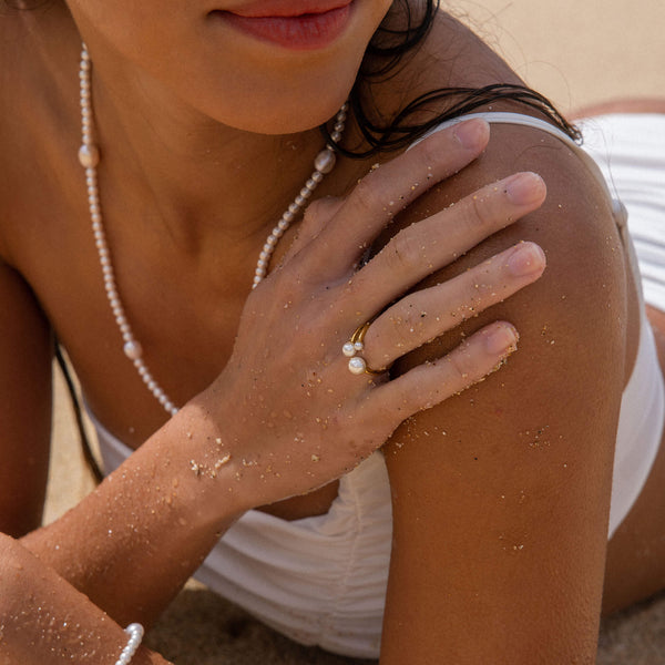 Perlenring und -kette von PURELEI, elegant und strahlend, am Strand getragen.