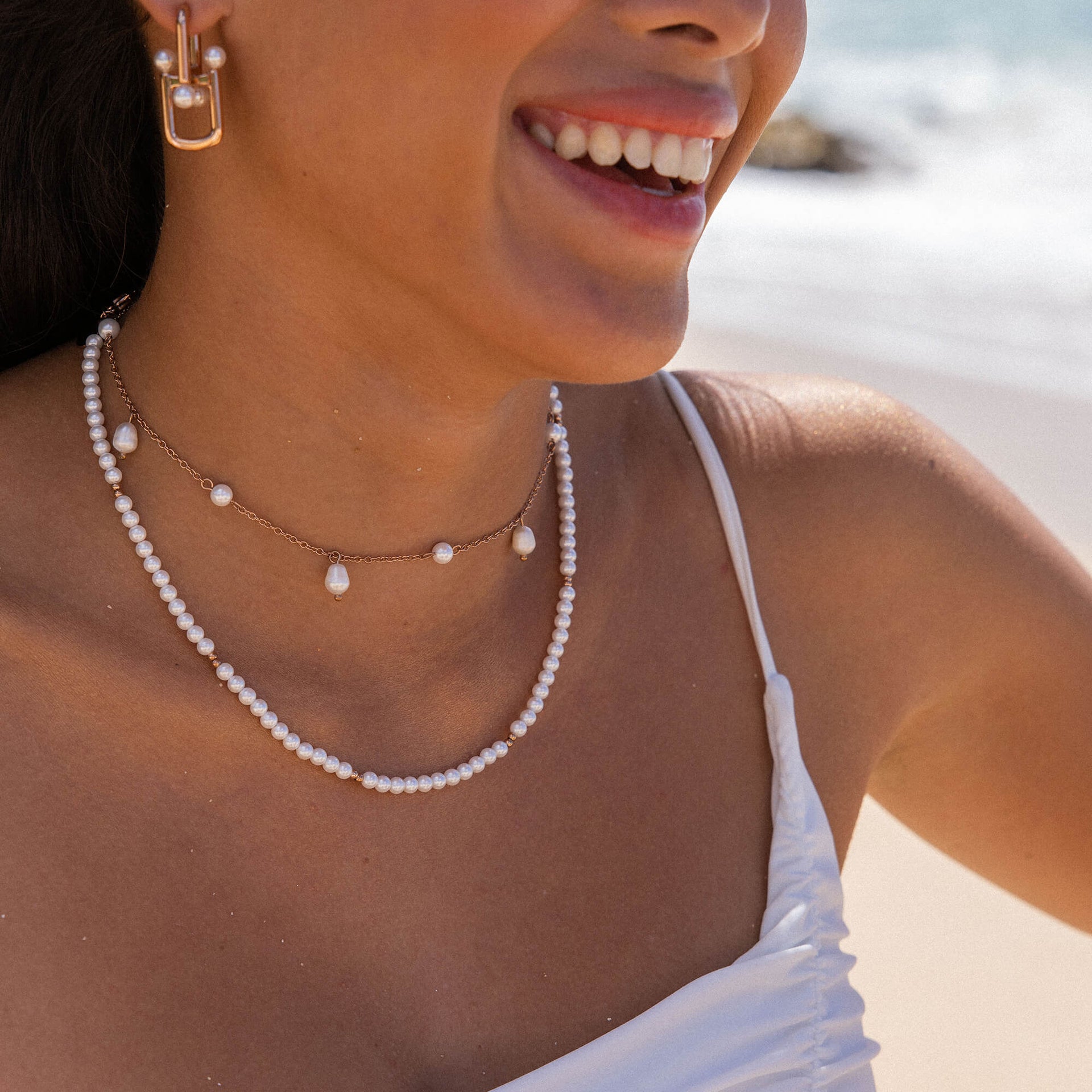 Zarte PURELEI Perlenkette und Ohrringe, strahlend am Strand getragen.