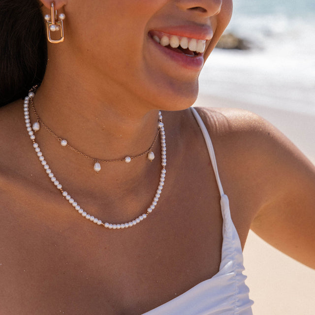 Zarte PURELEI Perlenkette und Ohrringe, strahlend am Strand getragen.