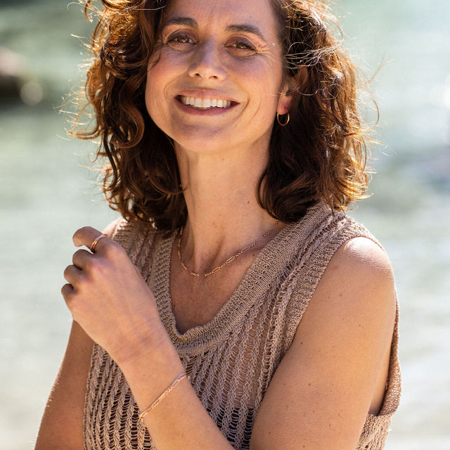 Zarte, goldene PURELEI Kette und Armband, getragen in sonniger, entspannter Atmosphäre.