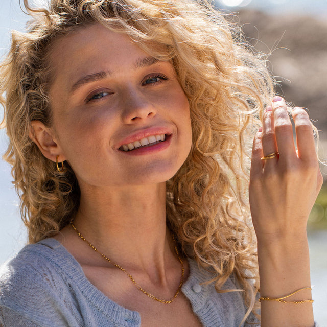 Goldene Kette und Ring von PURELEI, getragen mit einem Lächeln im Sonnenlicht.
