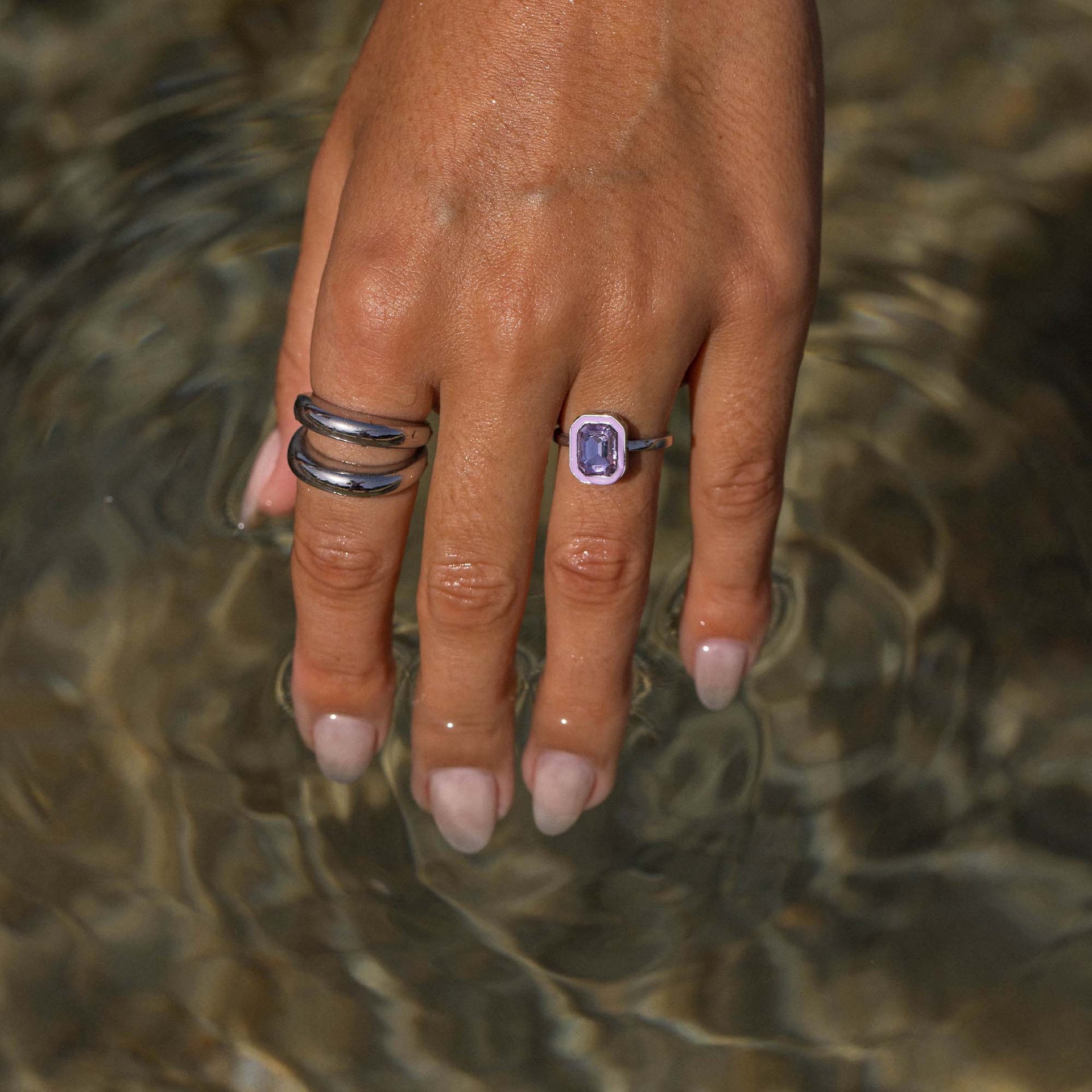 Dunkle Ringe aus Metall am Handgelenk, umgeben von Wasser, PURELEI-Design.