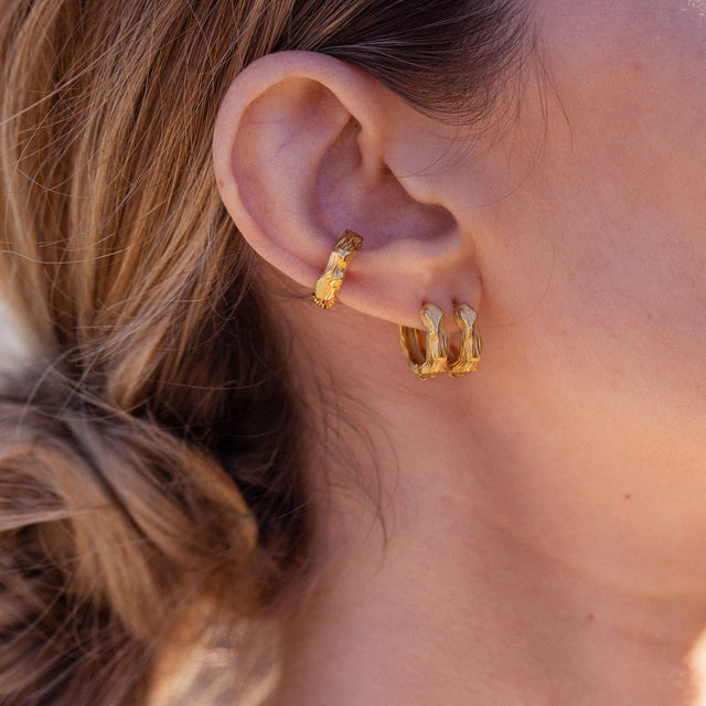 Goldene Creolen mit organischer Struktur, getragen am Ohr, von PURELEI.