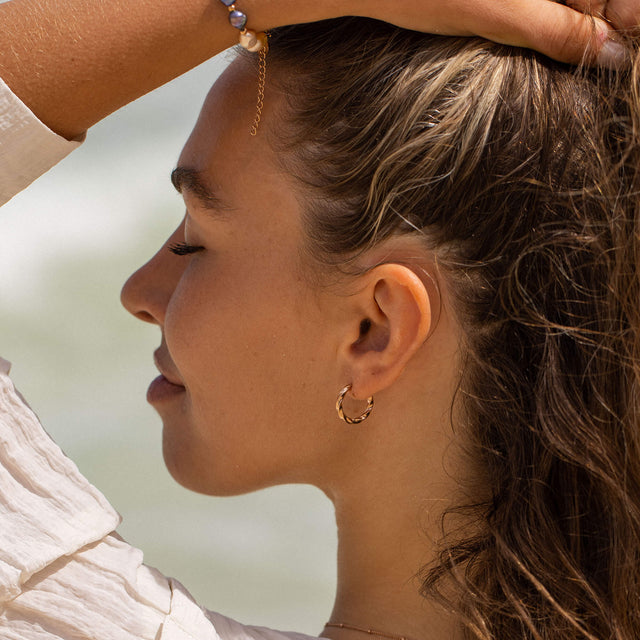 PURELEI Kelani Ohrringe aus goldvergoldetem Edelstahl mit gedrehtem Design getragen am Strand, feminin und elegant.