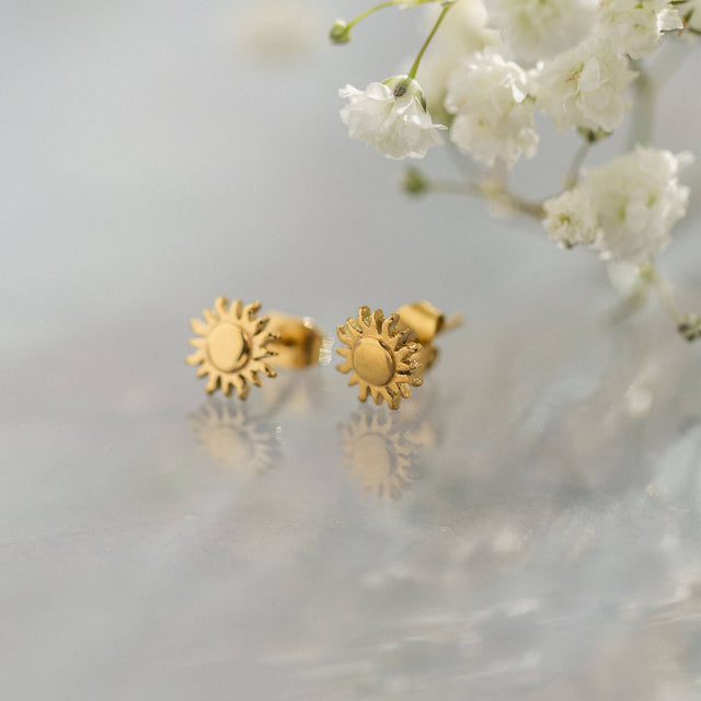 Goldene Ohrringe mit Sonnenmotiv von PURELEI, elegant und verspielt auf hellem Hintergrund.
