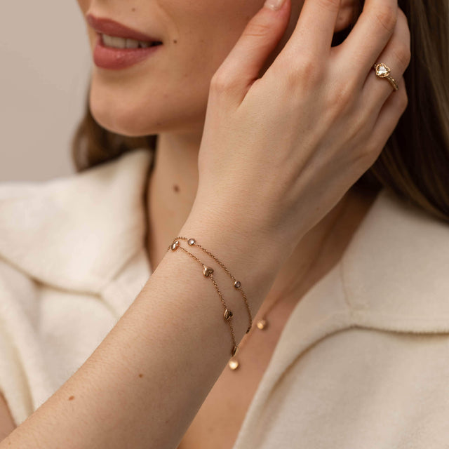 Roségoldenes Armband mit zarten Anhängern, getragen am Handgelenk, PURELEI Stil.