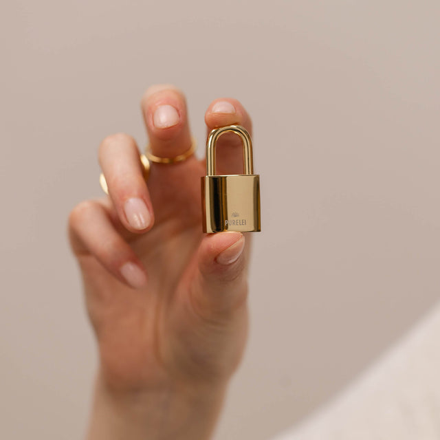 Goldener Anhänger in Form eines Schlosses, gehalten von einer Hand, PURELEI.