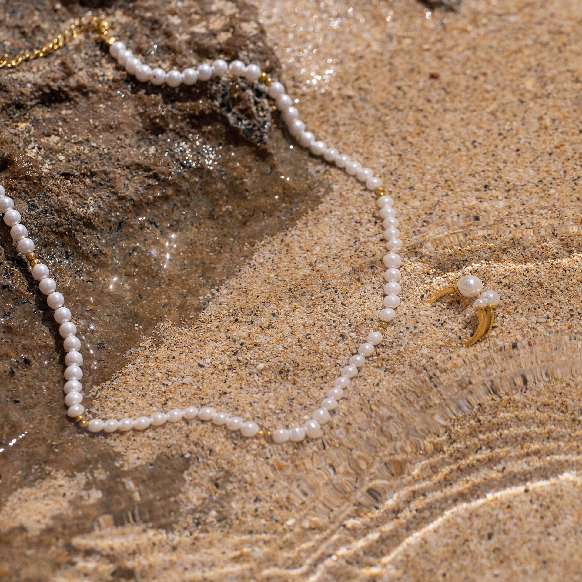 Finesse Ring von PURELEI mit zarten Seashell-Perlen und goldener Fassung, elegant auf Sandstrand inszeniert.