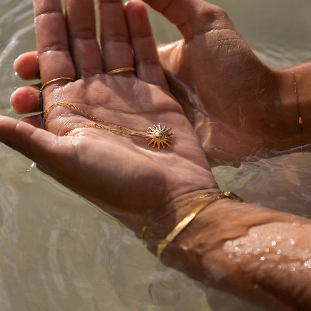 Sun Kette von PURELEI, goldene Edelstahlkette mit Sonnenanhänger, getragen im Wasser, strahlend und elegant.