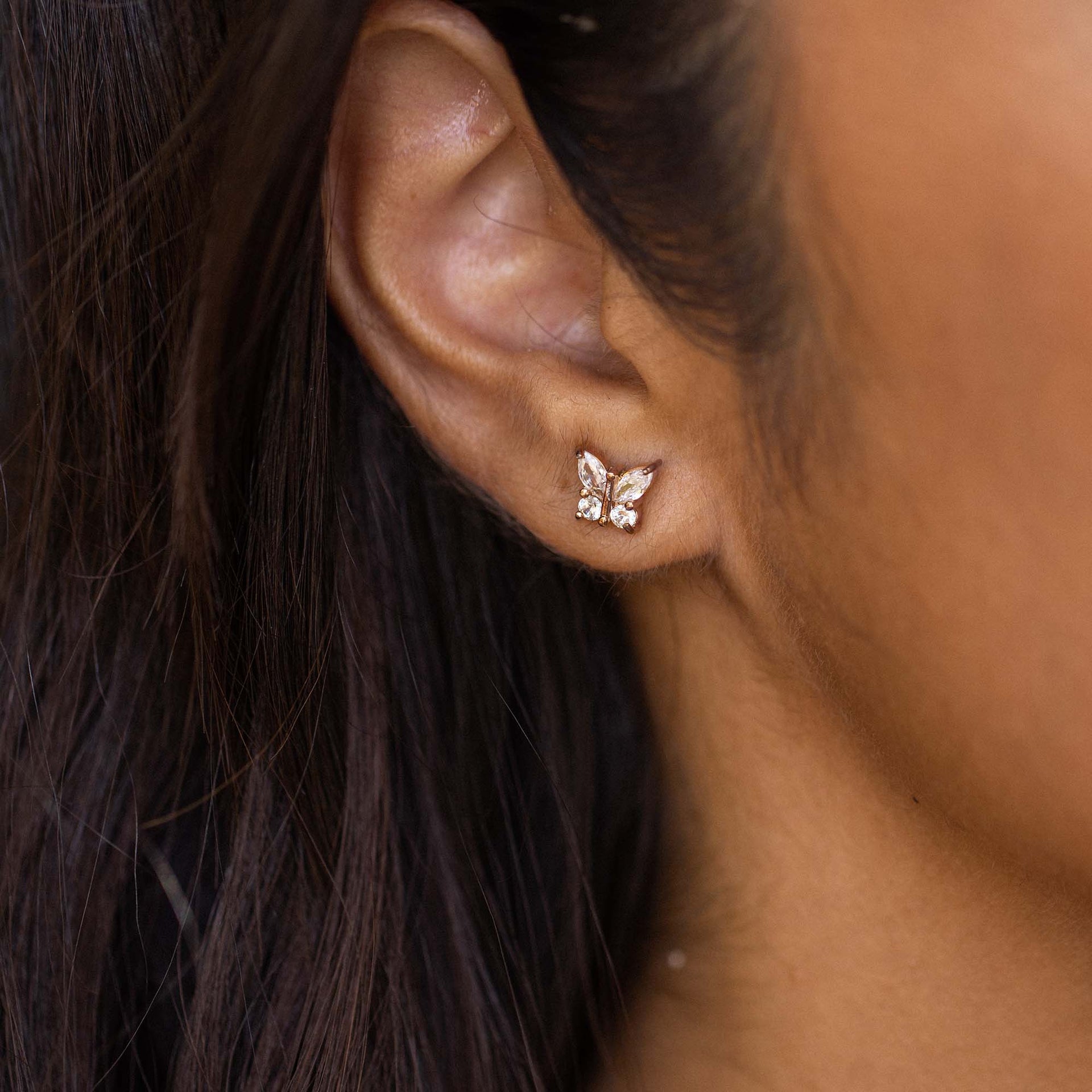 Roségoldene Schmetterling-Ohrringe von PURELEI, elegant und feminin am Ohr getragen.