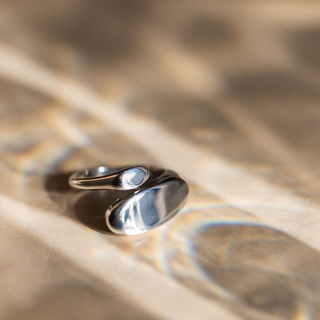 Silberner Ring mit geschwungenem Design auf sanftem Hintergrund, PURELEI inspiriert.