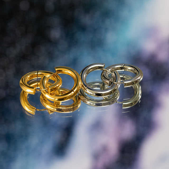 Glamorous Ohrringe von PURELEI aus Gold und Silber, poliert, elegant reflektierend auf glattem Spiegel.